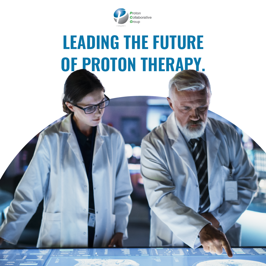 Two lab researchers in white coats reviewing equipment under a “Leading the Future of Proton Therapy” banner
