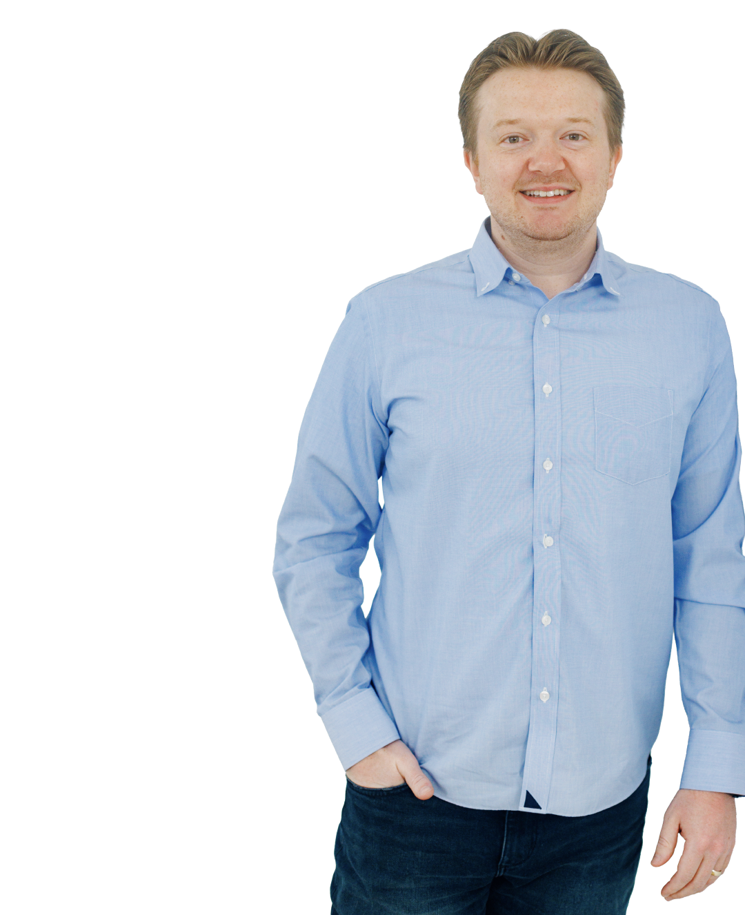 Smiling man in a light blue button-up shirt and dark jeans, standing against a white background.