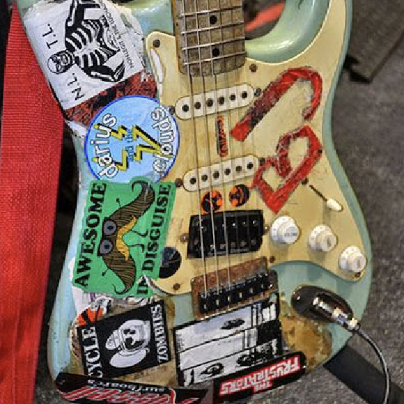 Sticker-covered cream electric guitar body with red paint and white knobs
