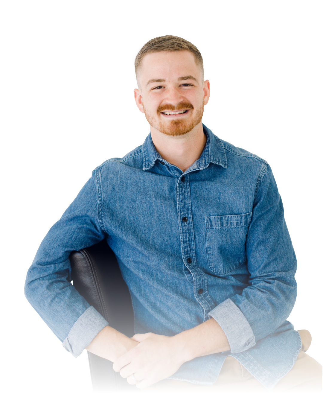 Smiling man in a blue denim shirt seated with arms folded on a white background