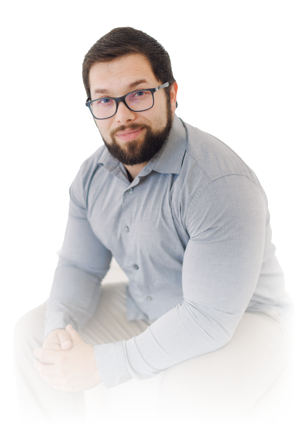 Man seated against a white background, wearing glasses and a light gray shirt, looking at the camera