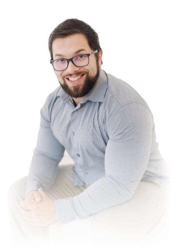 Smiling person with glasses and beard, seated in a light gray shirt against a white background