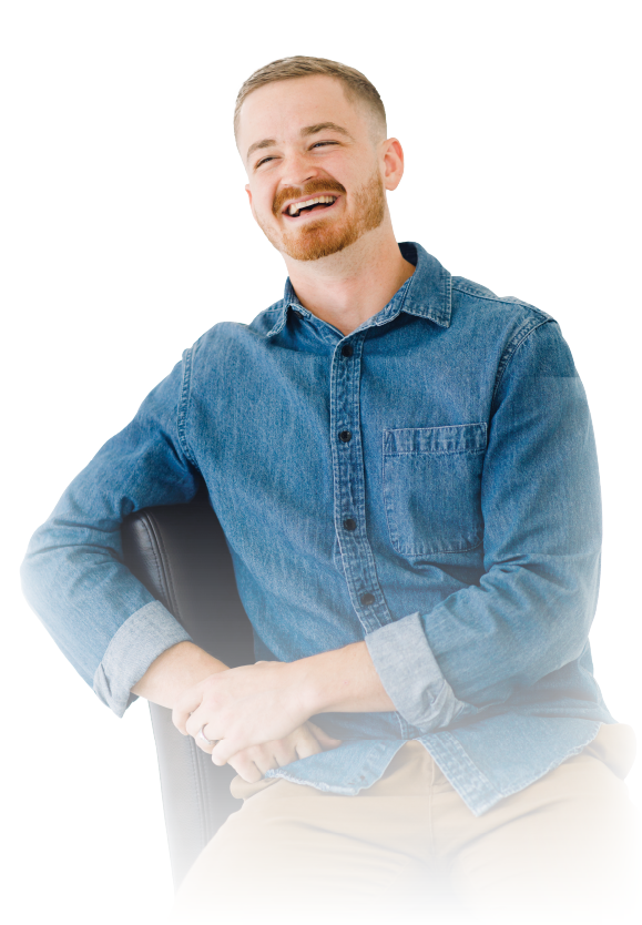 Smiling man in a blue denim shirt sitting with folded hands against a white background