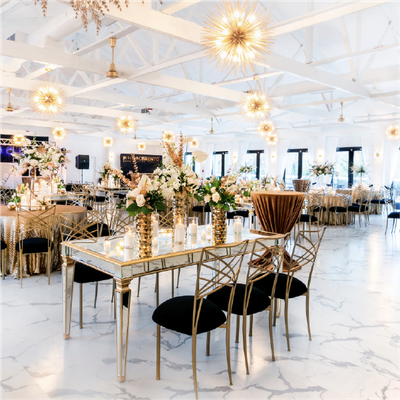 Elegant white event venue with gold decor, floral centerpieces, and mirrored tables set for a formal reception