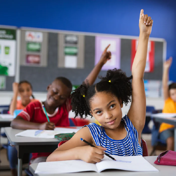 Students in a classroom, one girl raising her hand while others work at desks