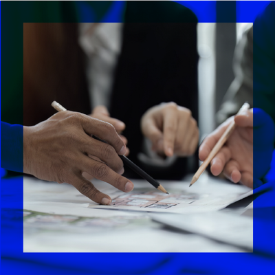Three people point pens at documents during a business meeting.