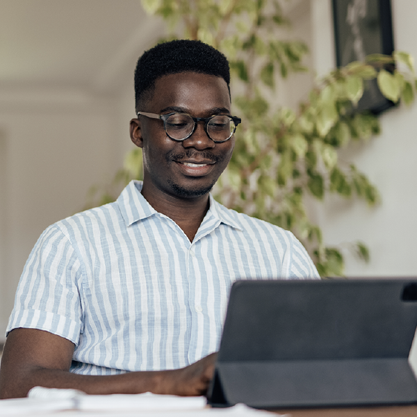 Person smiling while using a laptop at a table in a bright room