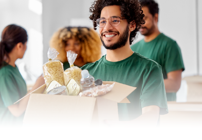 Person smiling and holding a box of food donations in a bright room