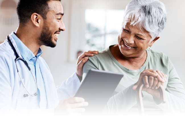 Doctor reviewing a tablet with an older patient, both smiling in a bright clinic.