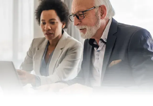 Two coworkers in business attire discussing documents at a bright office desk