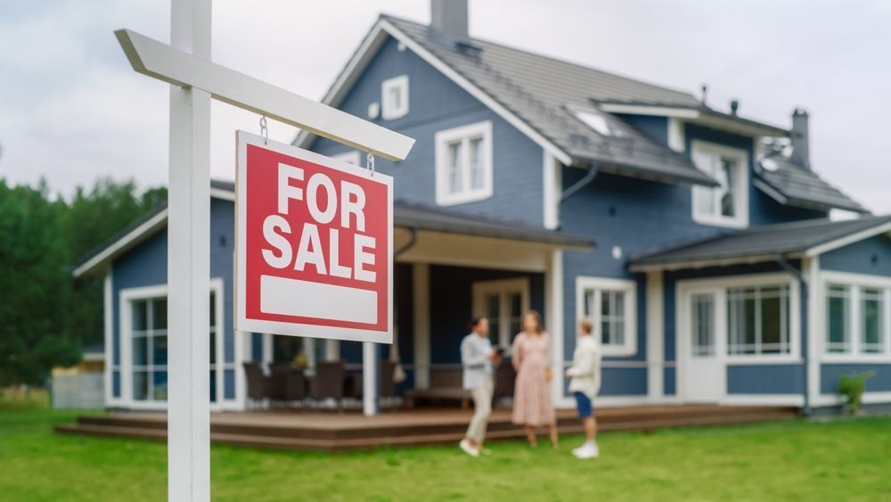 For sale sign in front of a blue house with two people standing on the lawn