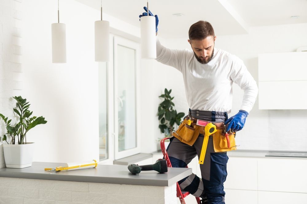 Handyman measuring a kitchen counter while wearing a tool belt and gloves in a bright modern kitchen