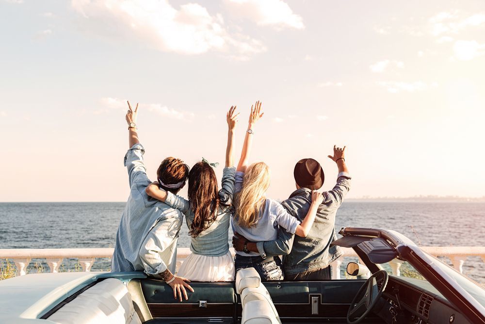 Four friends with raised arms enjoy a sunset boat ride on the open sea.