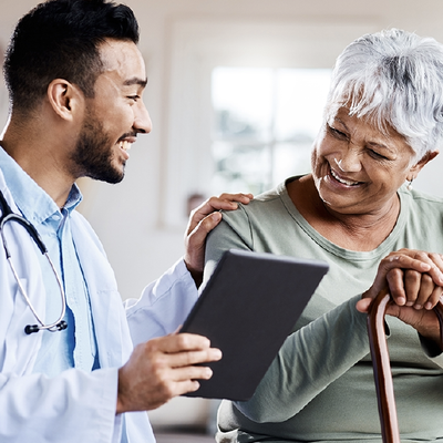 Doctor showing tablet to smiling patient with cane in a bright clinic