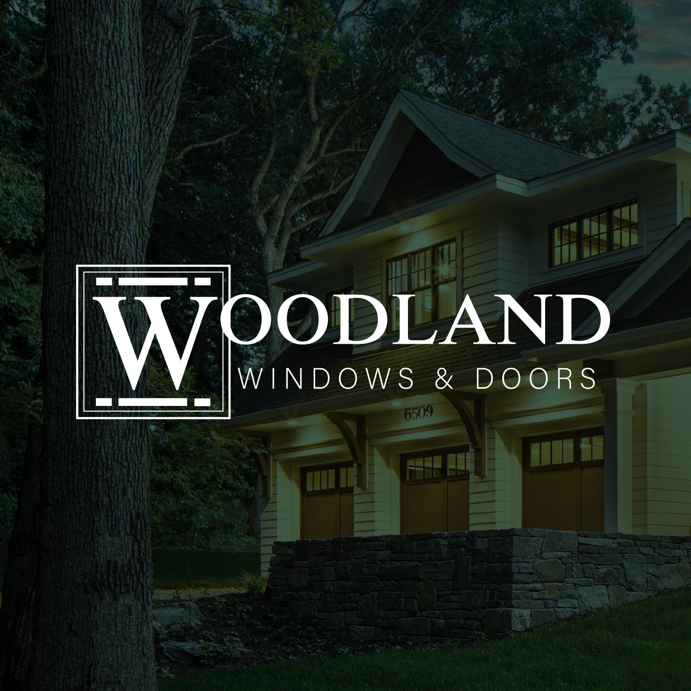 WOODLAND Windows & Doors logo over a house at dusk with trees and stone foundation