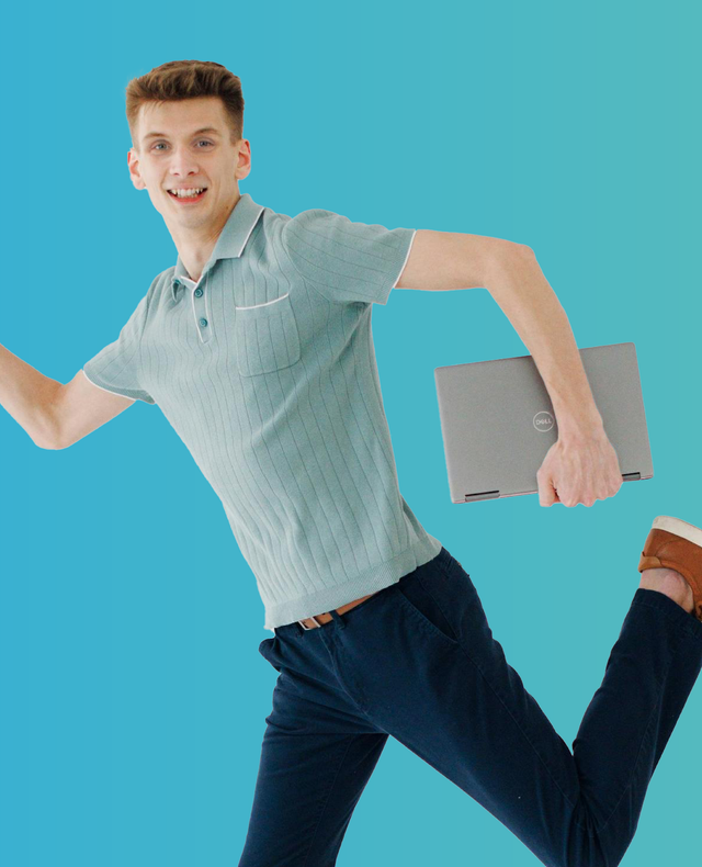 Person in a light blue shirt and dark jeans jumping while holding a gray laptop on a turquoise background