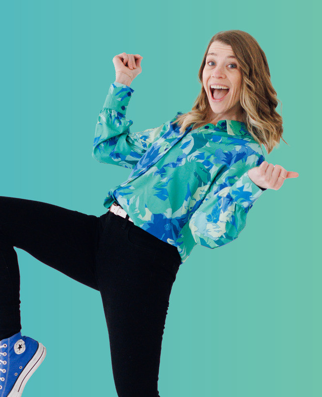 Person posing playfully in a blue patterned top and black pants against a teal background