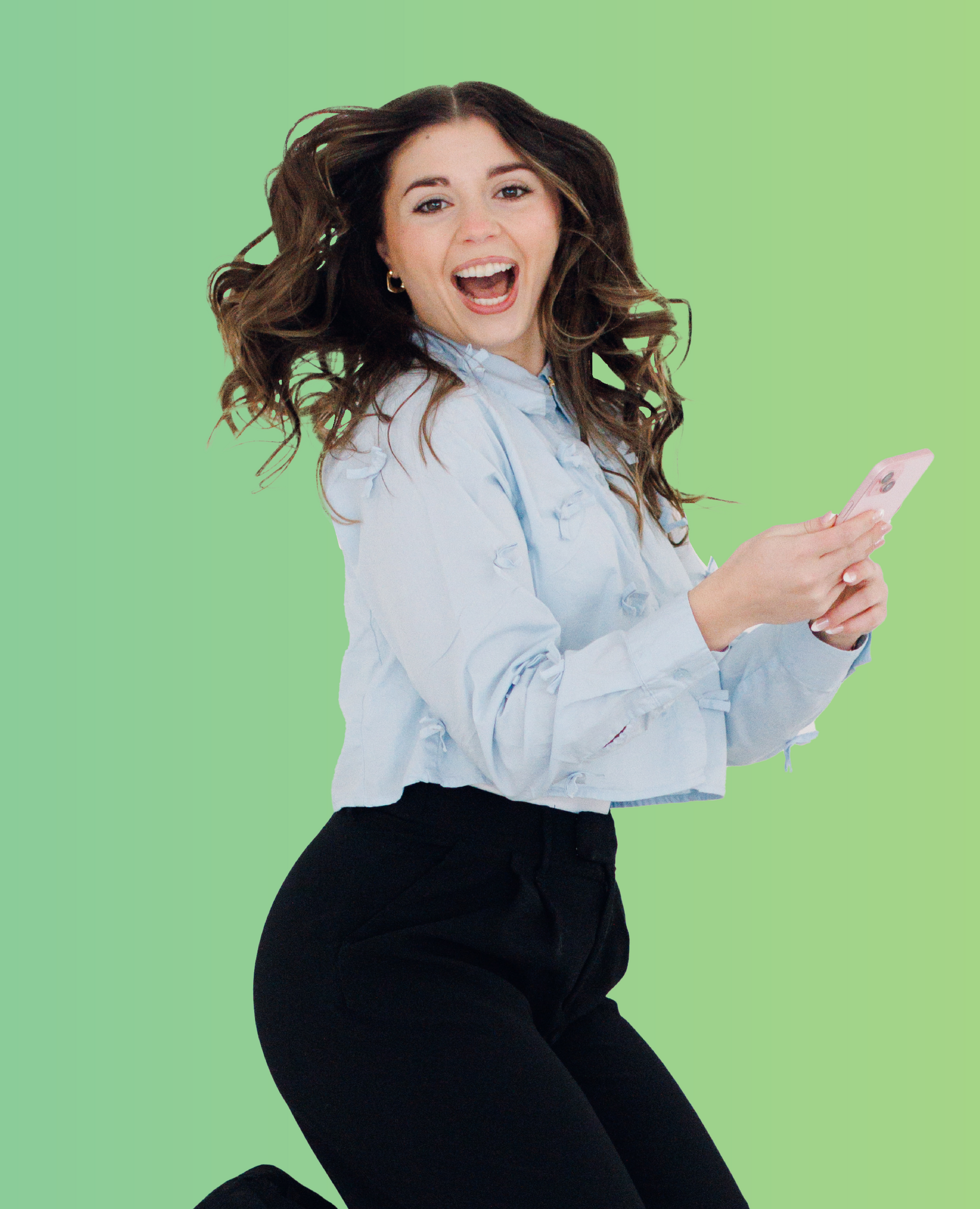 Smiling woman in a light blue shirt posing against a green background, holding a phone
