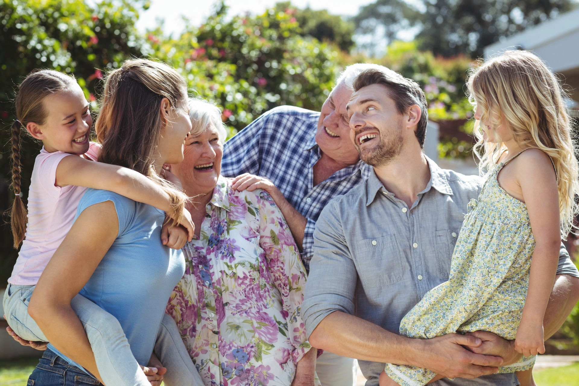 Family of six laughing outdoors, two children being held.