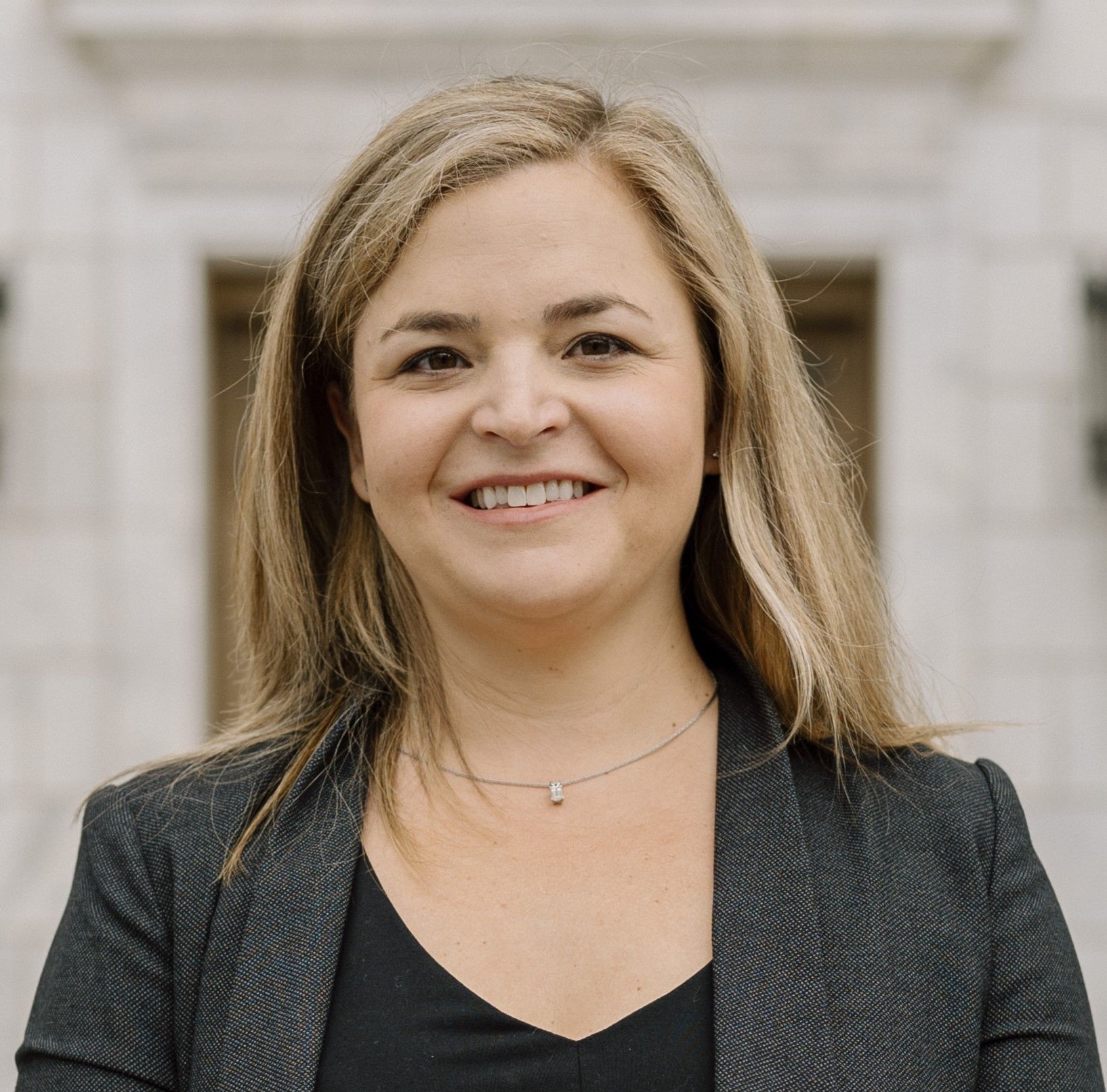 Woman in a dark blazer smiling in front of a stone building.