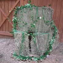 Two hay bales stacked, decorated with green tinsel for a festive occasion, against a wooden door.