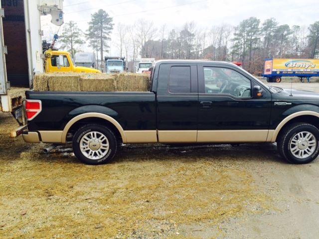 Black Ford pickup truck with tan accents, loaded with hay bales.