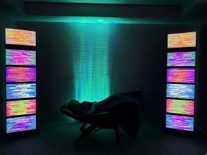 A person is laying in a chair in front of a wall of televisions.