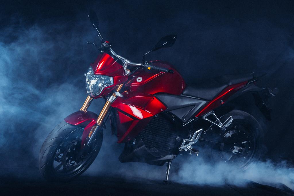 A red Urban S electric motorcycle is sitting in the dark with smoke coming out of it.