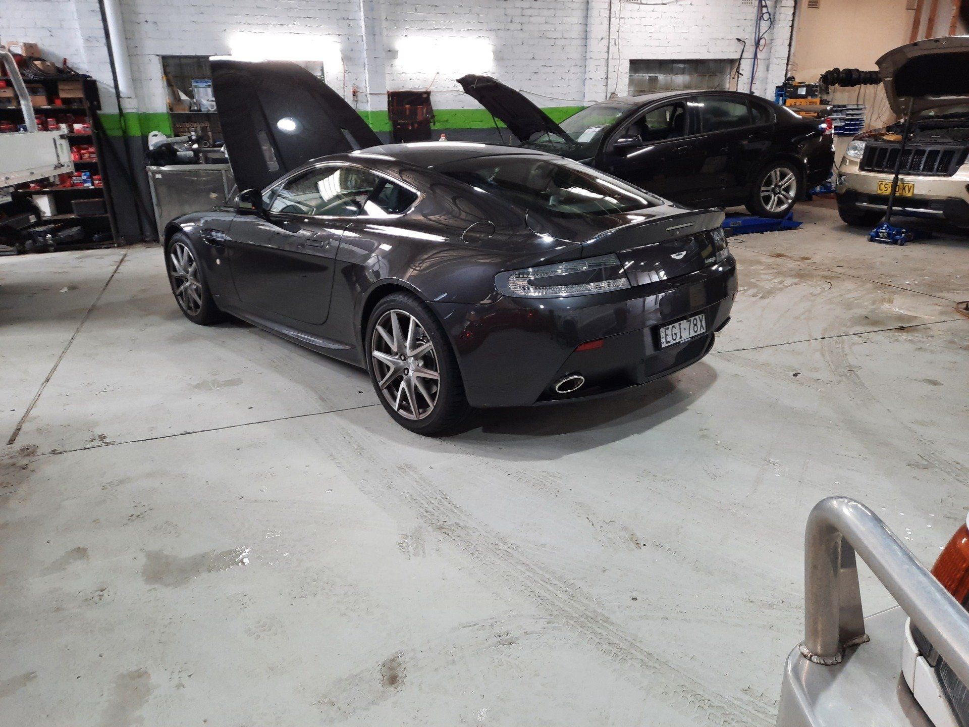 A black car is parked in a garage with its hood up.