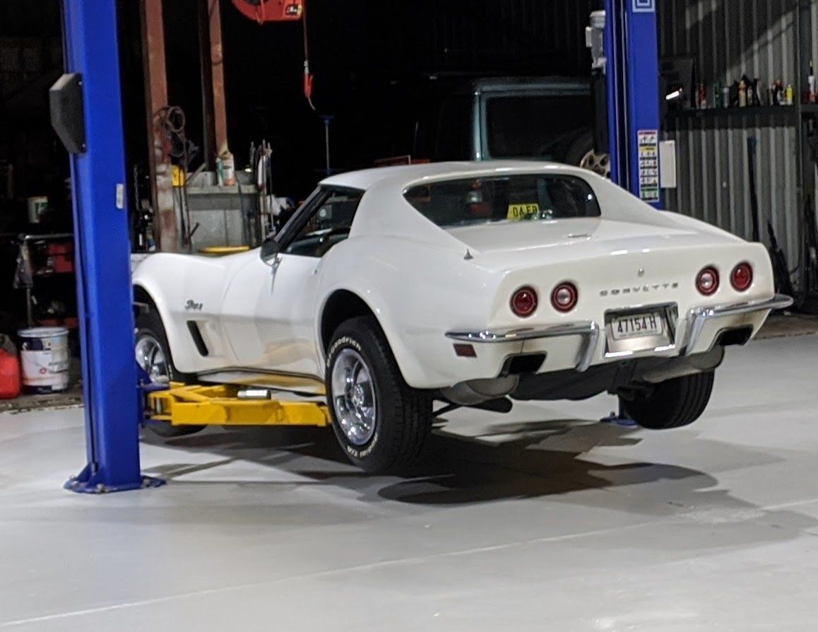 A white corvette is on a lift in a garage