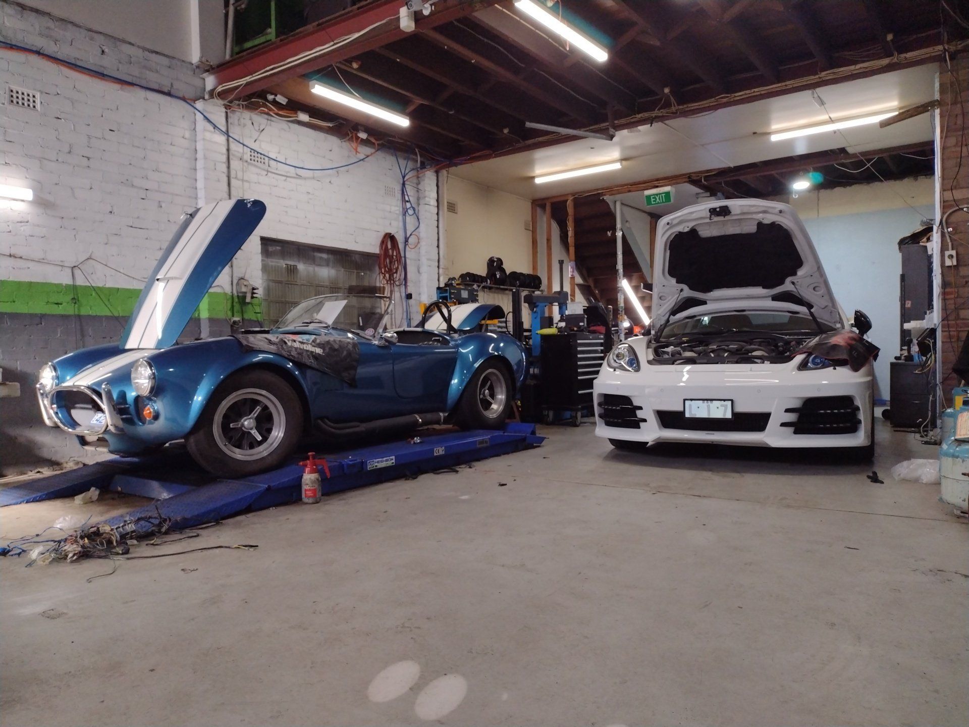 Two cars are parked in a garage with their hoods open.