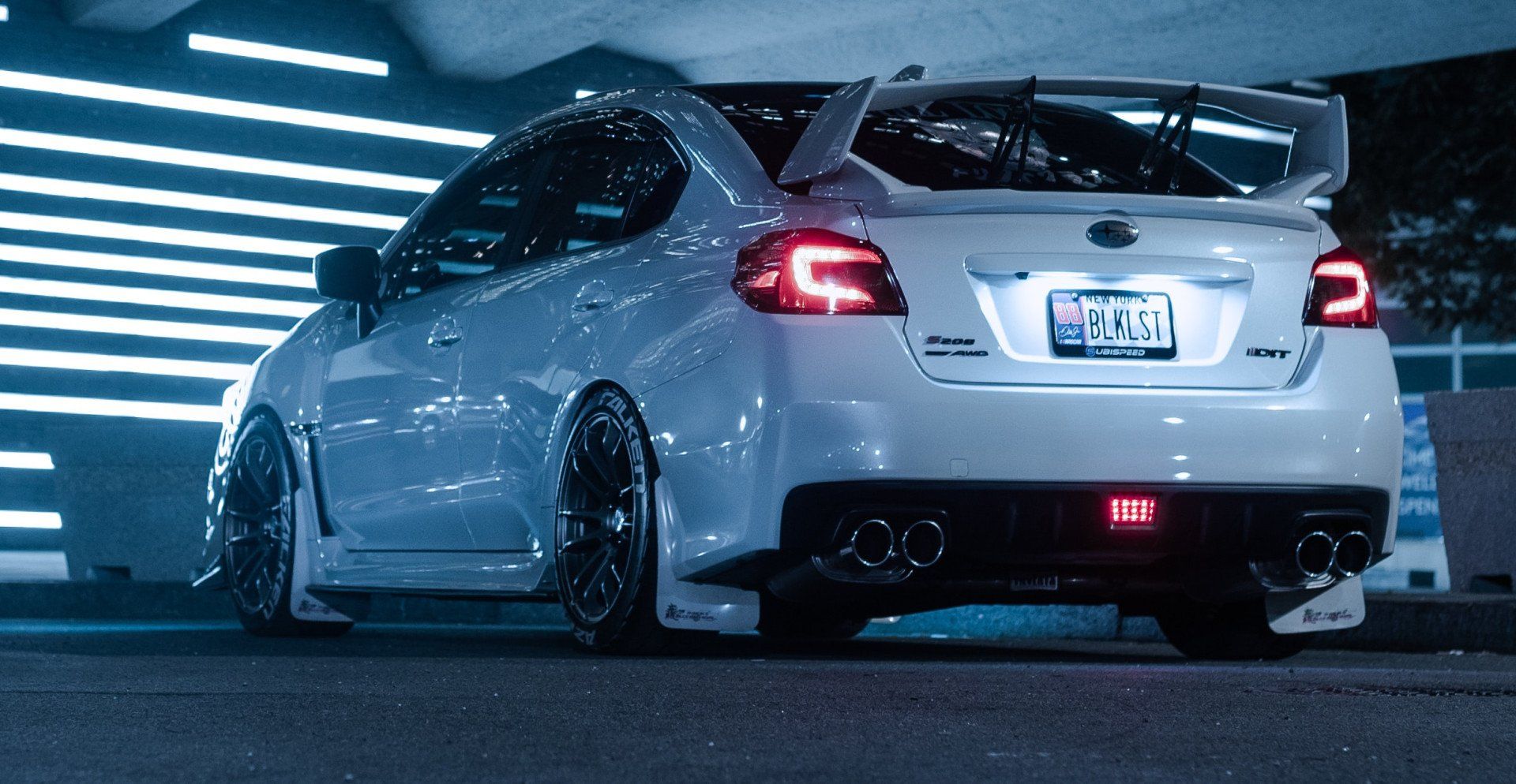 A white subaru wrx sti is parked in a parking garage at night.