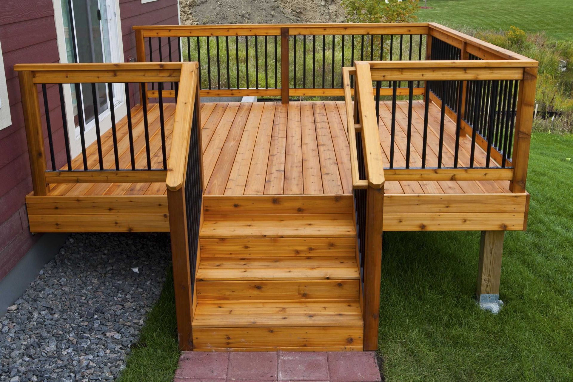 Wooden deck with stairs, railing, and balusters. Brown wood with a green grass background.