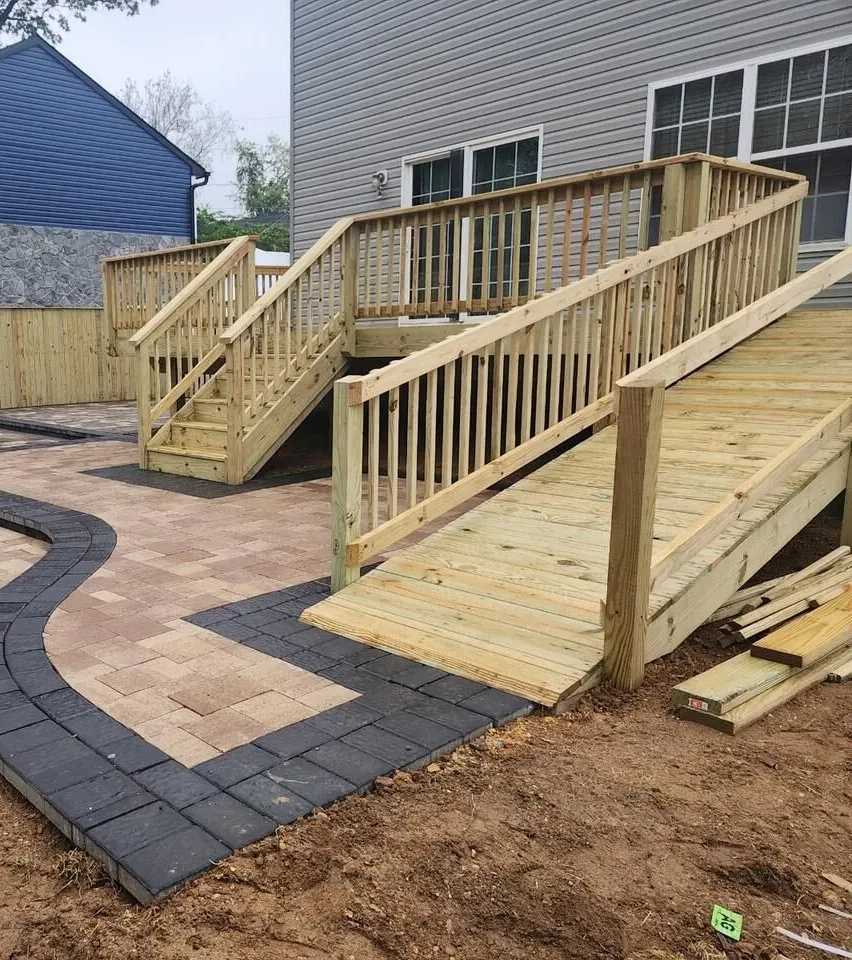 Custom wooden deck with stairs and ramp leading to a brick patio.