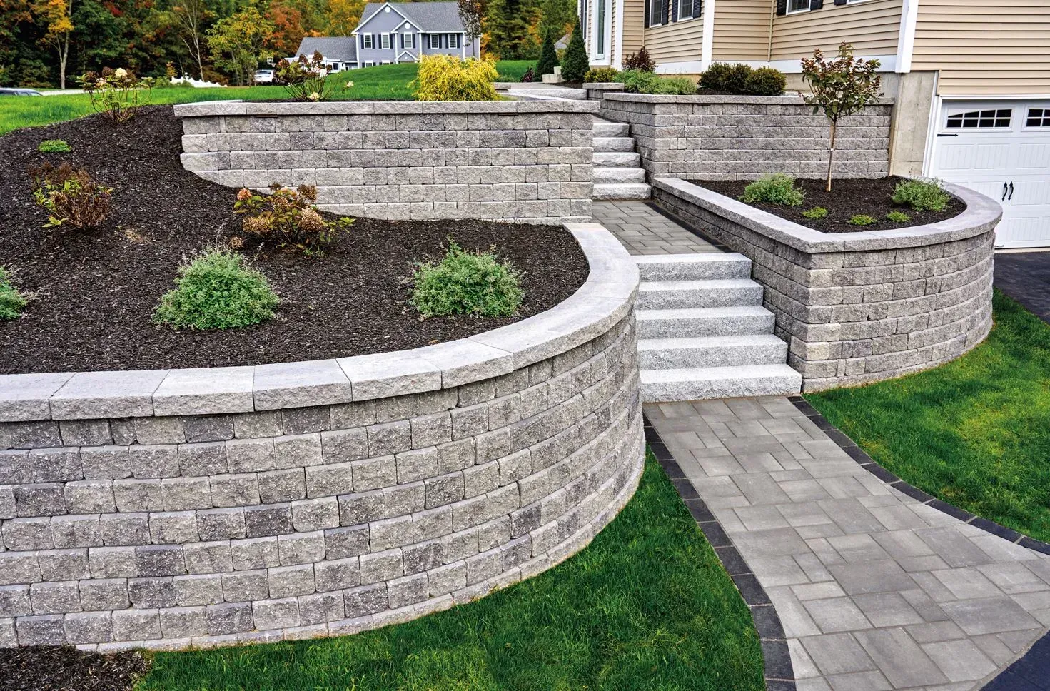 Stone retaining walls and steps leading up to a house with a garage; landscaped yard with a walkway.