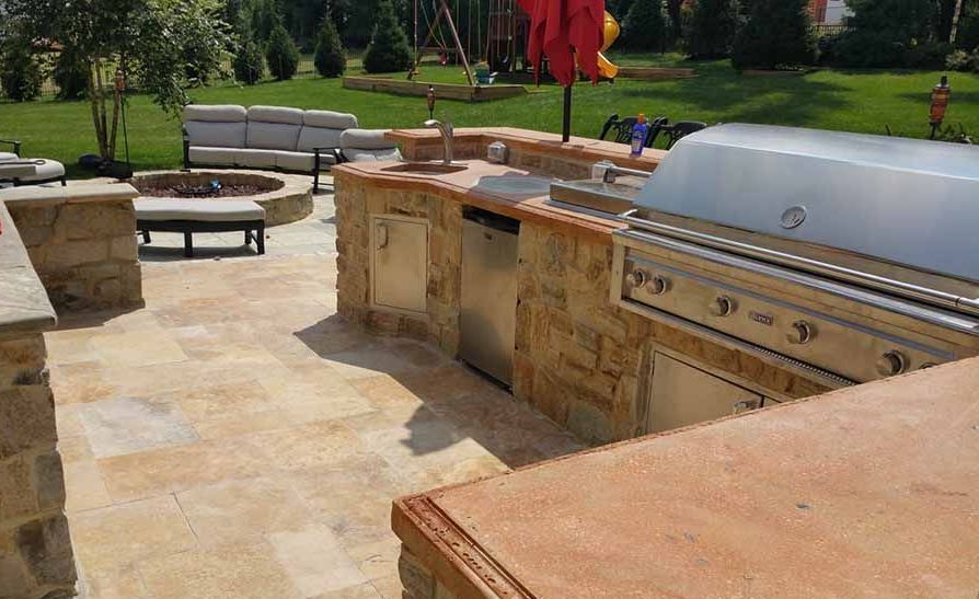 Outdoor patio with stone grill, countertop, and seating in a landscaped backyard.