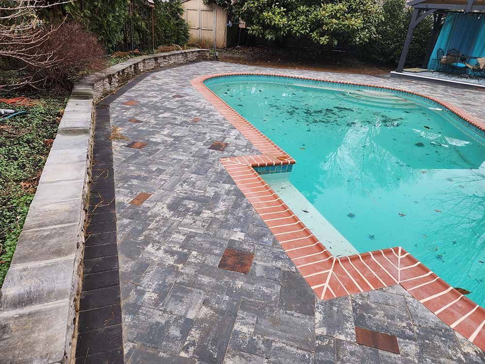A large swimming pool with a brick walkway surrounding it