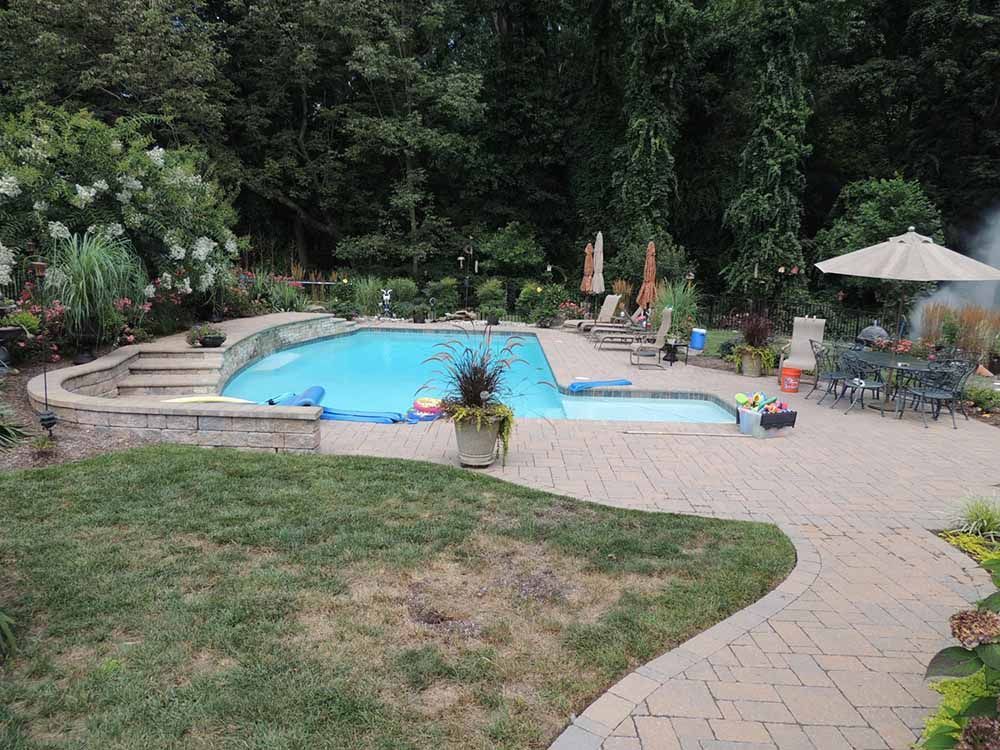 A large swimming pool in a backyard with a patio and umbrellas.