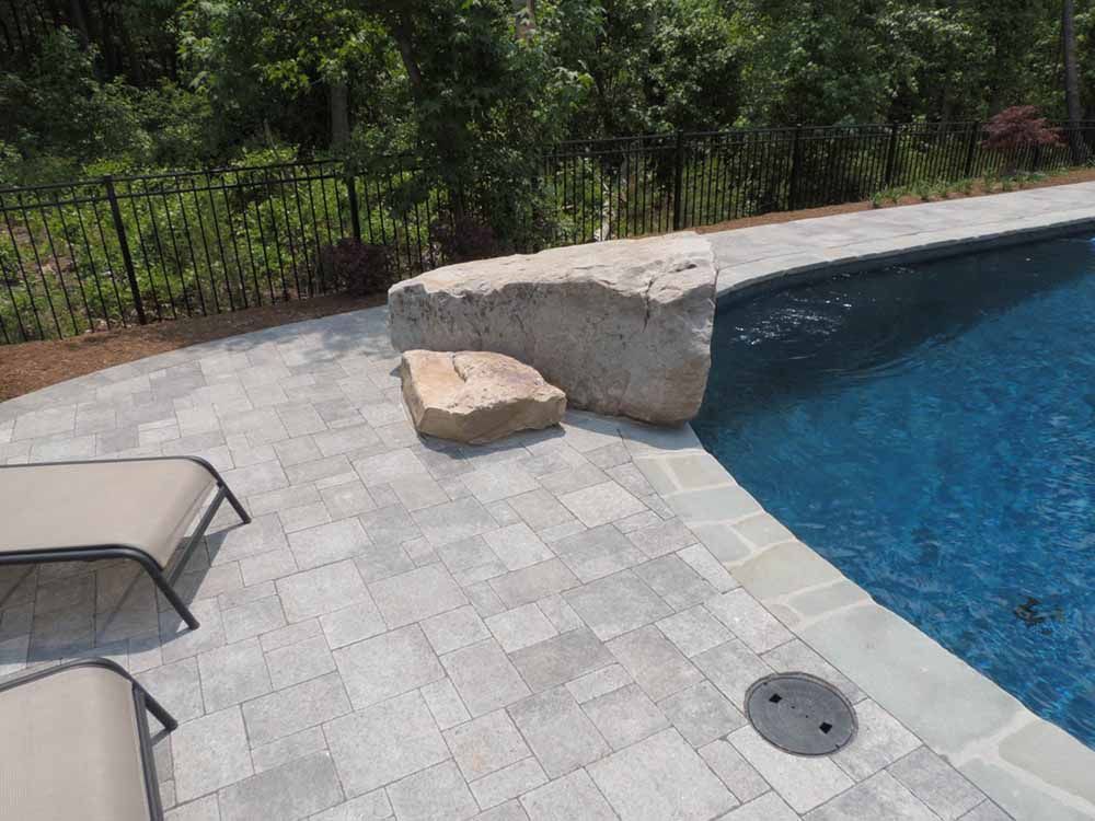 A large rock is sitting on the edge of a swimming pool.