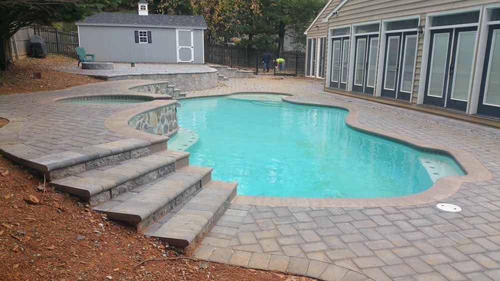 A large swimming pool with stairs leading to it is in the backyard of a house.