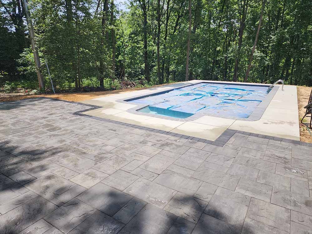 A large swimming pool is surrounded by trees and a patio.