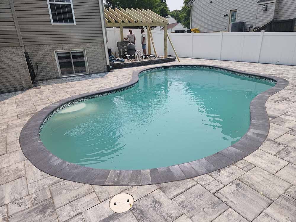 A large swimming pool is surrounded by a brick patio and a white fence.