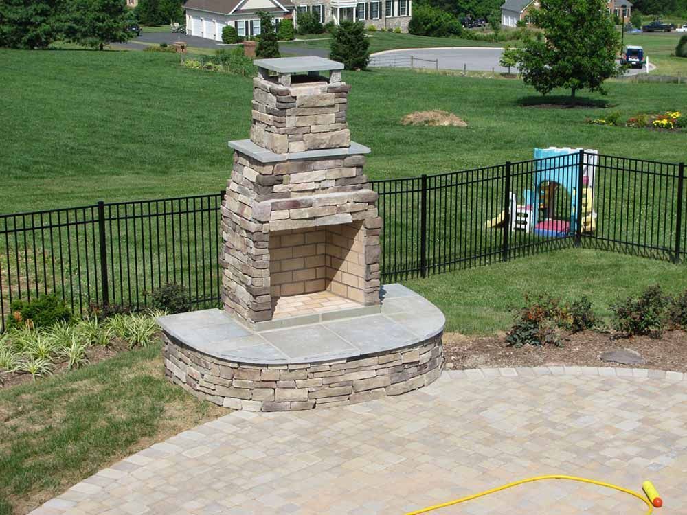 A stone fireplace in a backyard with a fence around it