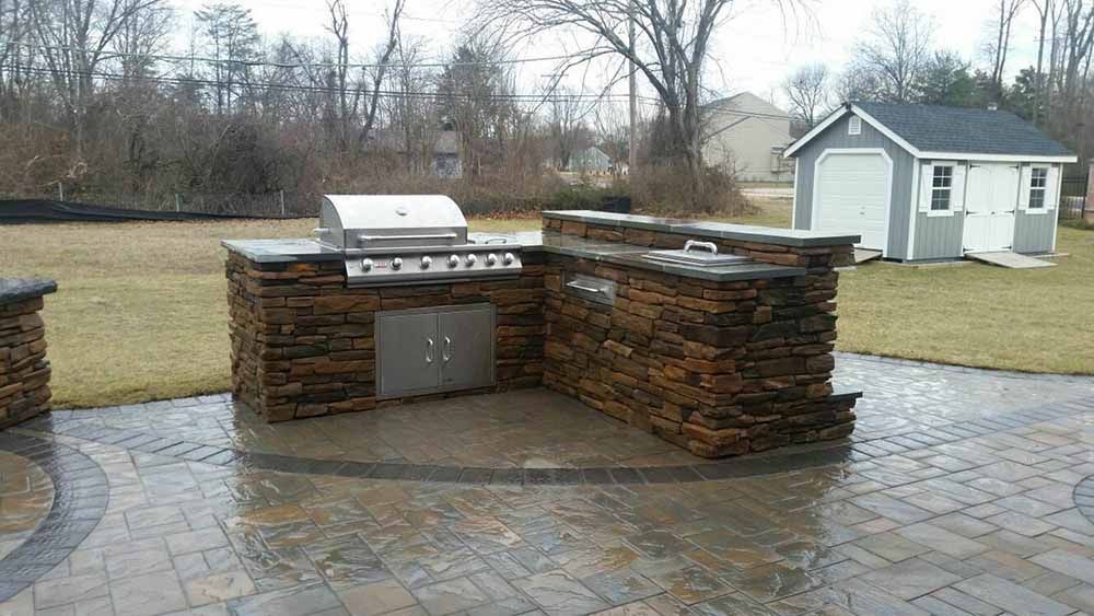 A patio with a grill and a shed in the background