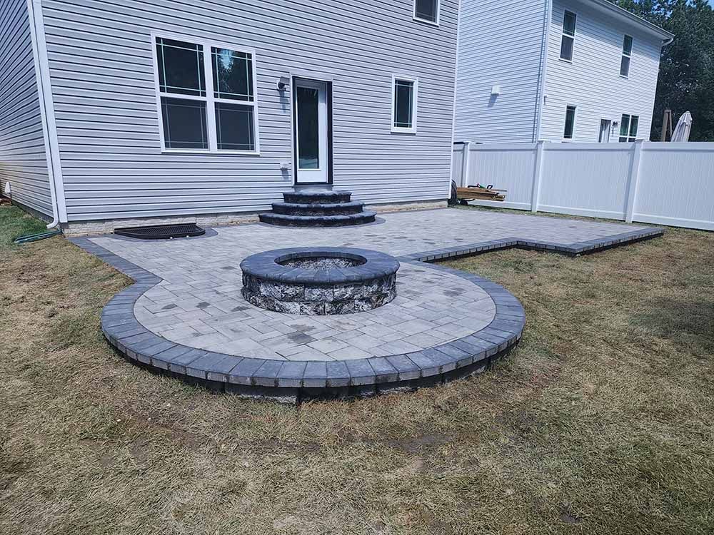 A fire pit is in the middle of a patio in front of a house.