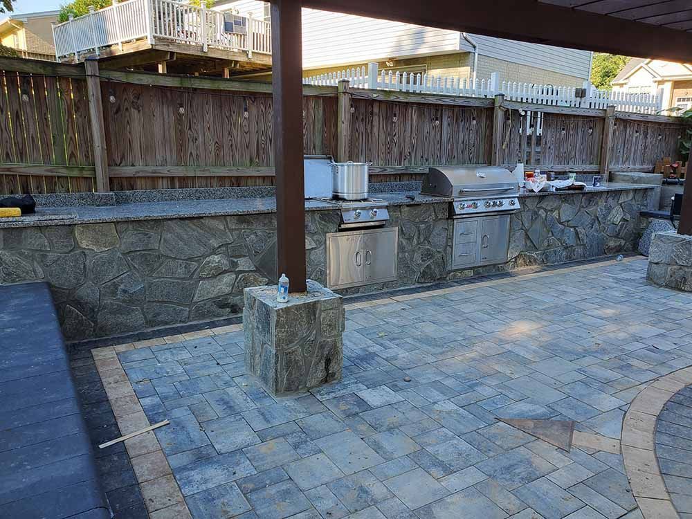 A large outdoor kitchen with a grill and a wooden fence in the background.
