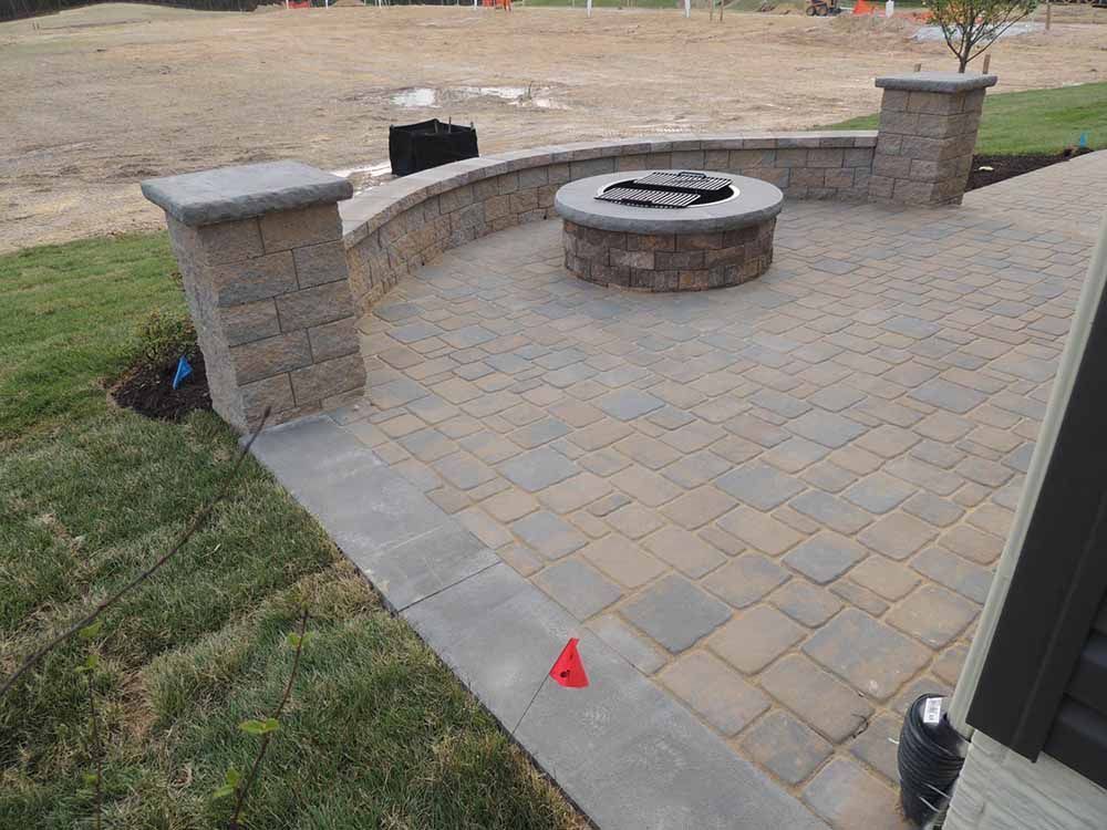 A brick patio with a fire pit in the middle as well as a retaining wall in the back yard of Maryland resident