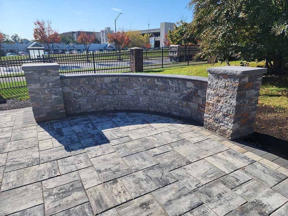 A patio with a stone wall and a fence in the background.