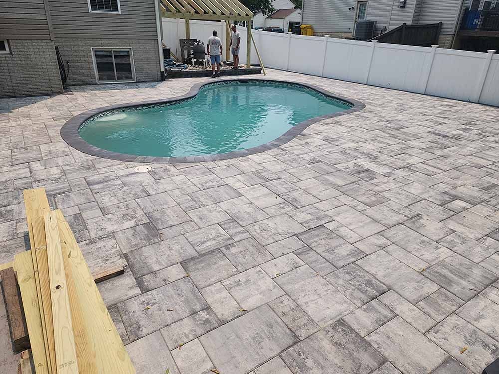 A man is standing next to a swimming pool in a backyard.