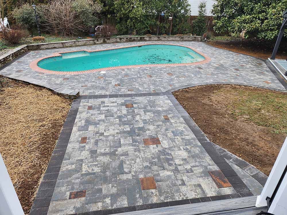 A large swimming pool is surrounded by a brick patio.